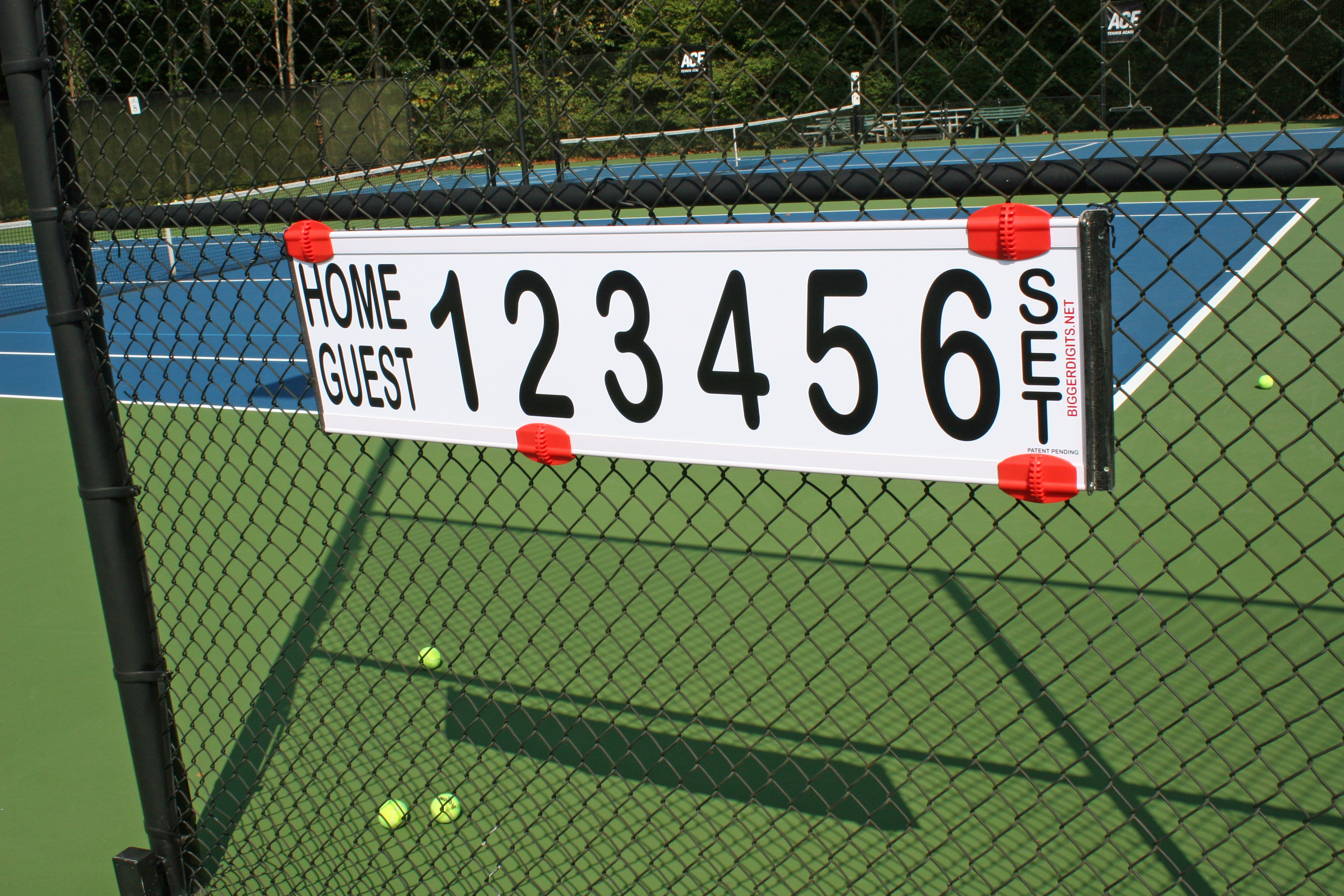 Fence mounted tennis scoreboard clipped to a chain-link fence on a tennis court, showing Home/Guest and numbers 1–6.