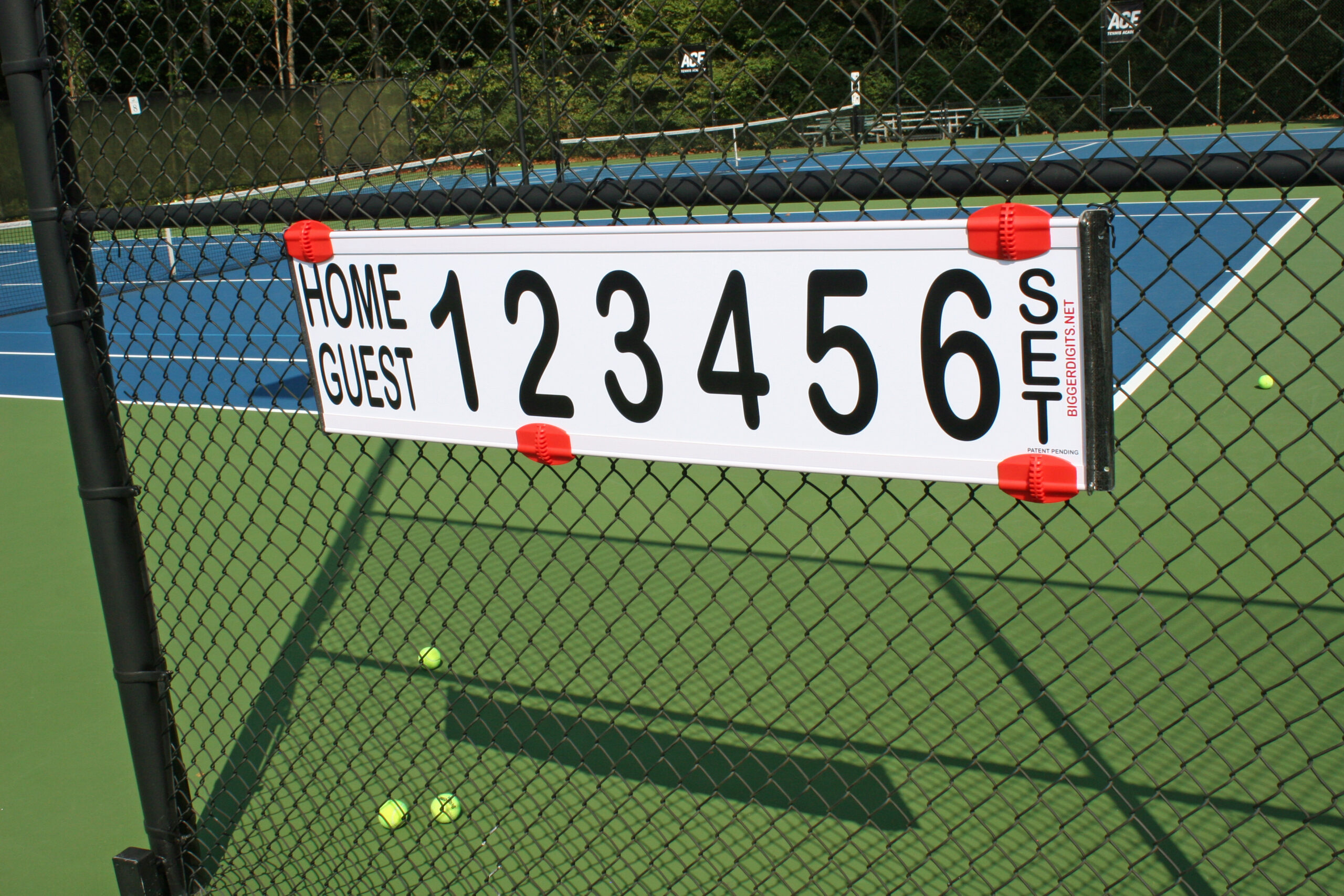 Scoreboard on a tennis court showing 1-6 with home/guest labels; fence, nets, and tennis balls on the court. How to keep score in tennis context.